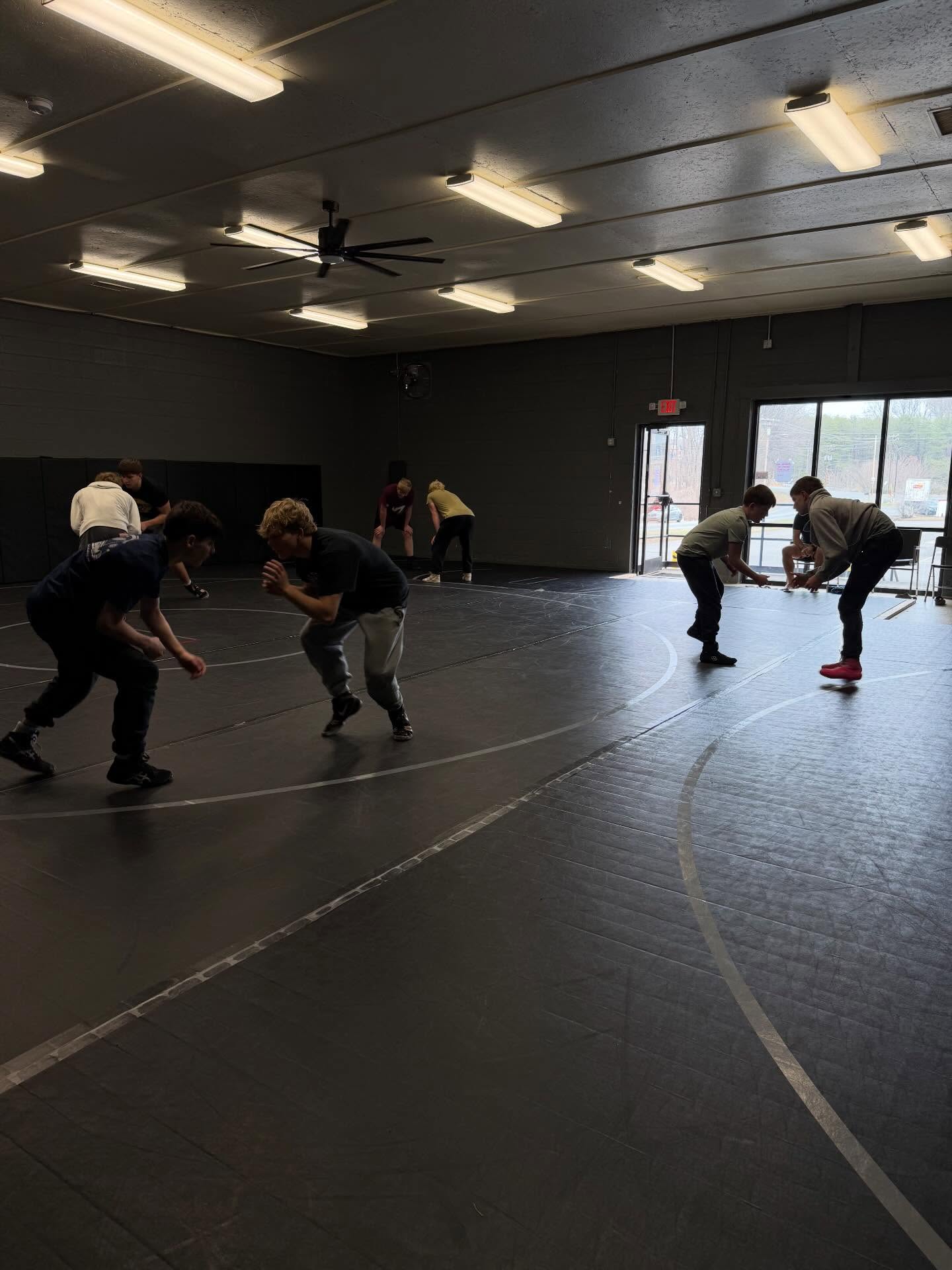 Athletes drilling takedowns in daylight near the front windows.