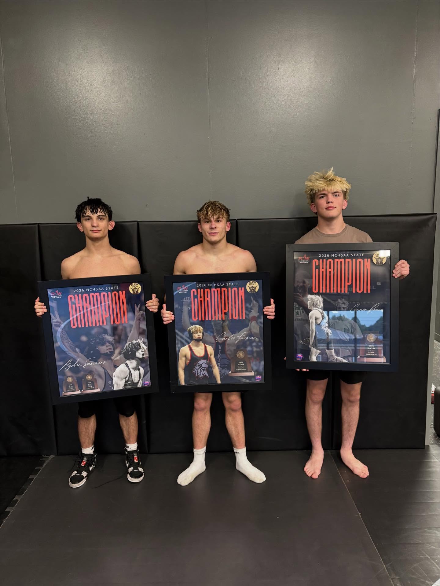 Three Raw West wrestlers holding framed 2026 NCHSAA state champion plaques.