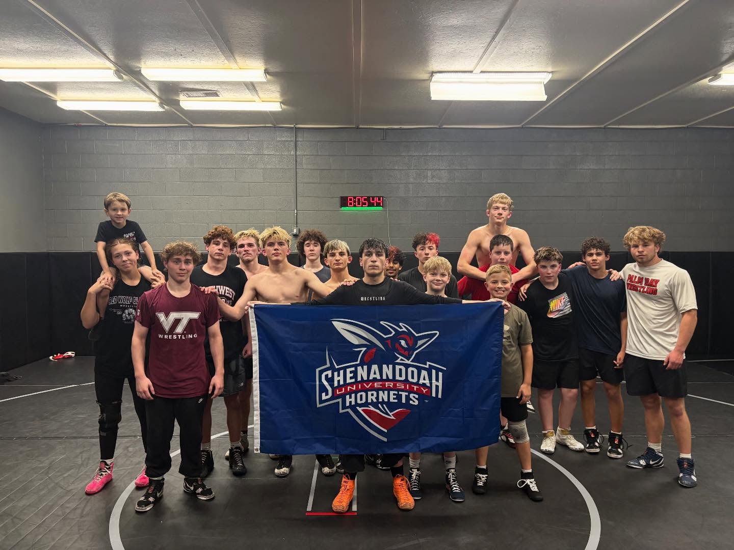 Raw West athletes holding a Shenandoah University Hornets flag in the wrestling room.